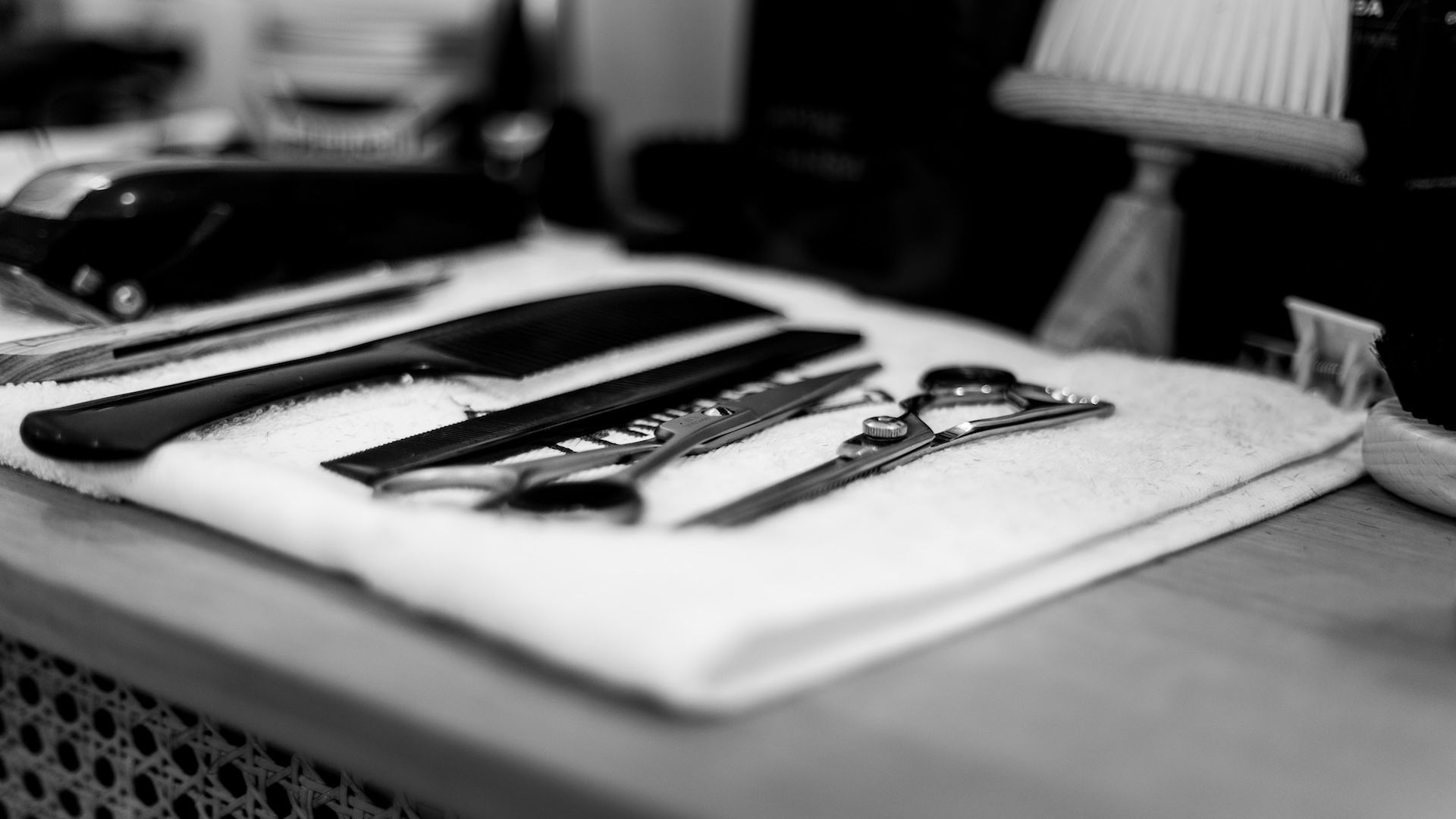 Barber tools on a towel: clippers, shears, comb, and straight razor. Black and white.