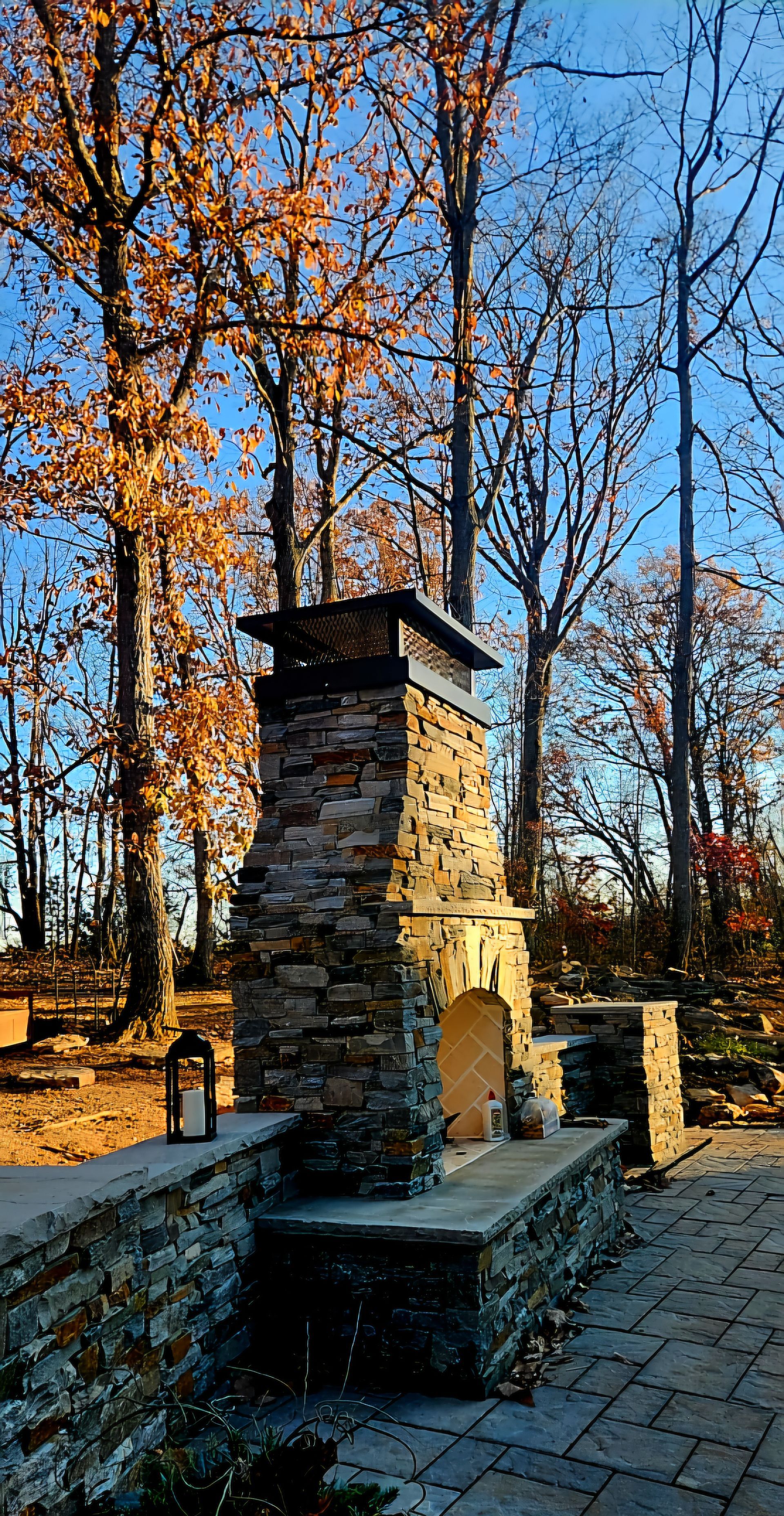 A stone fireplace chimney cap in the middle of a forest with trees in the background.