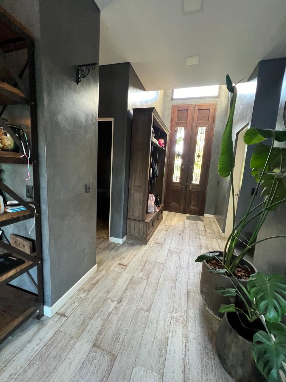 Recibidor con paredes grises, estanterías de madera y puerta de entrada de madera. 