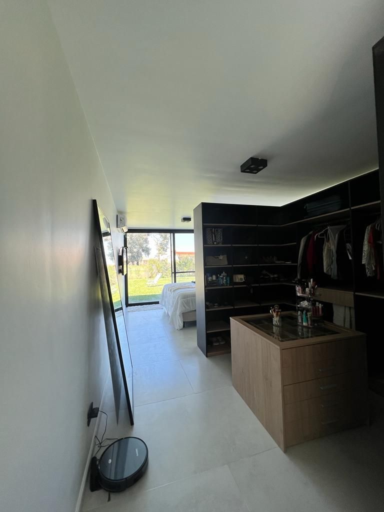 Moderno vestidor con estantes abiertos, espacio para colgar ropa y una isla central. Paredes blancas, mucha luz.