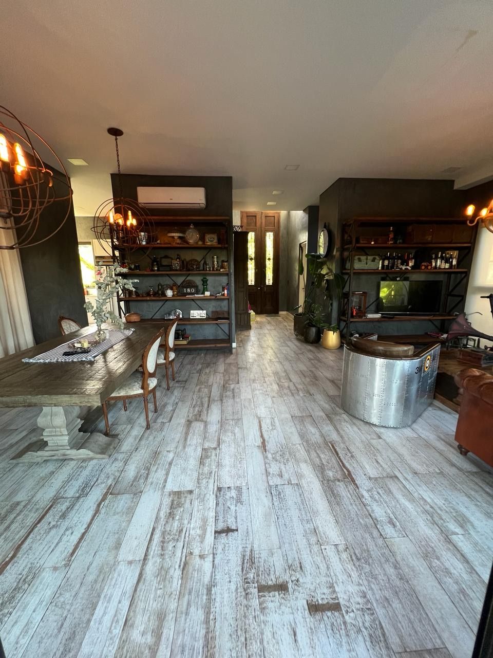 Amplia sala de estar con suelos de madera envejecida, estanterías y mesa de comedor.