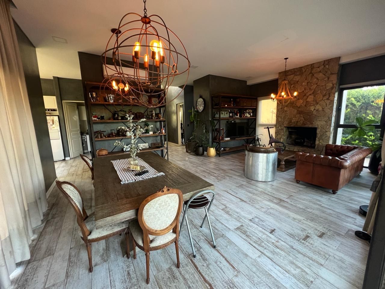 Espacio diáfano con zona de comedor, estanterías, chimenea y sofá de cuero; decoración rústica e iluminación tenue.