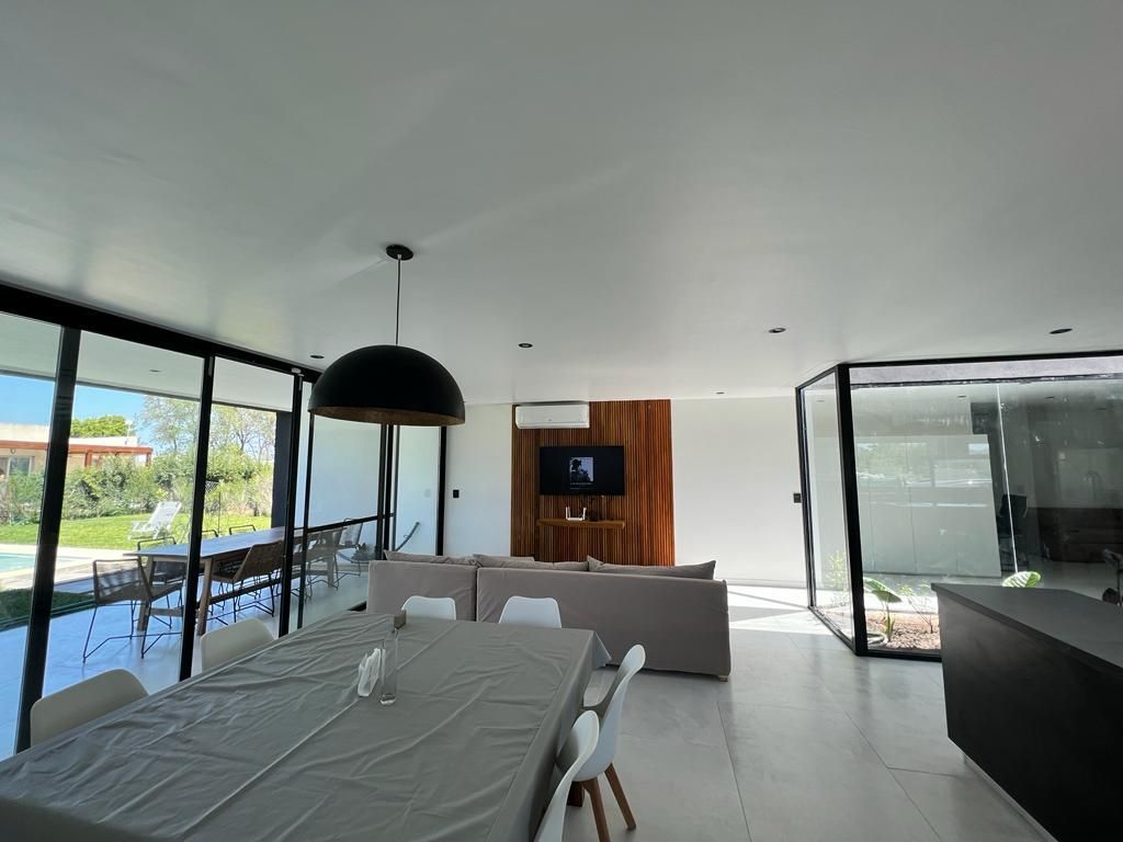 Salón moderno con paredes de cristal, mesa de comedor y sofá. El televisor está montado sobre un panel de madera.
