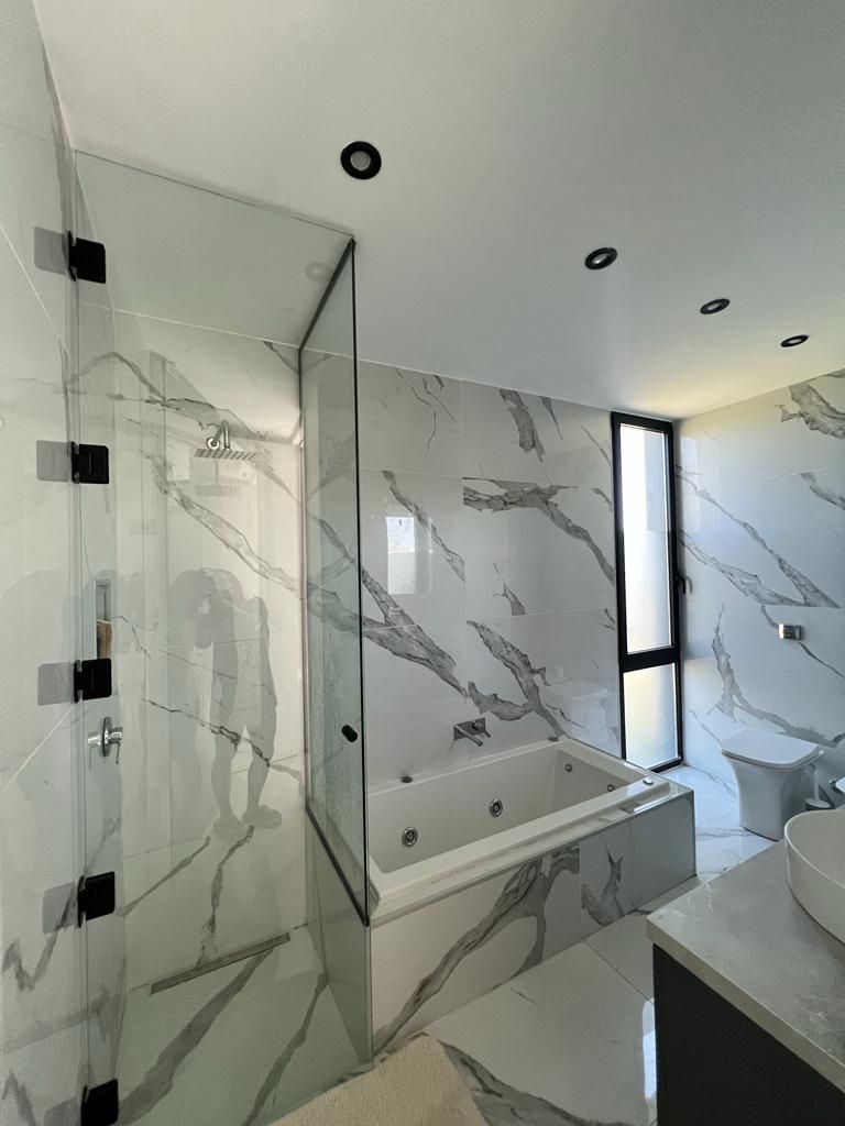 Baño moderno con paredes con aspecto de mármol, ducha de cristal, bañera y ventana.