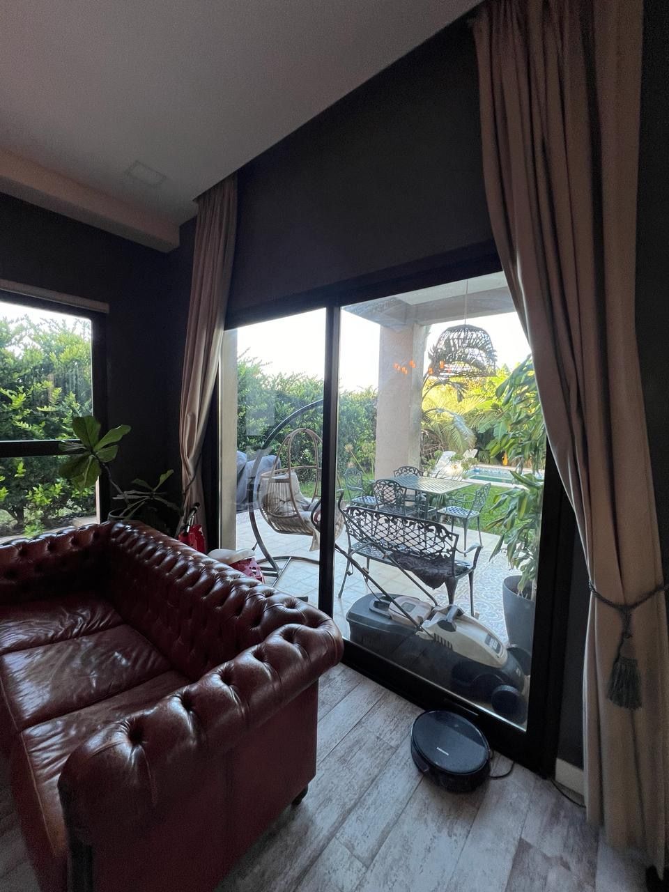 Sofá de cuero rojo junto a una gran ventana con vistas a un patio amueblado y con vegetación.