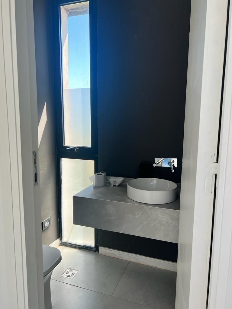 Baño moderno con lavabo de encimera gris y pared negra. Un gran ventanal deja entrar la luz del sol.