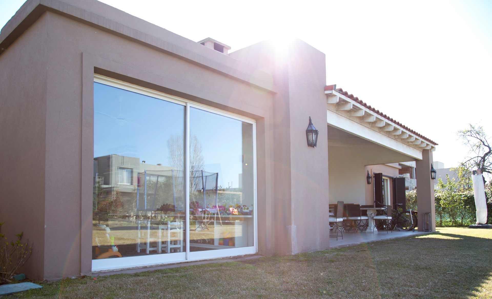 Casa de estuco color canela con grandes puertas corredizas de vidrio, patio cubierto y césped verde. Mucha luz solar.