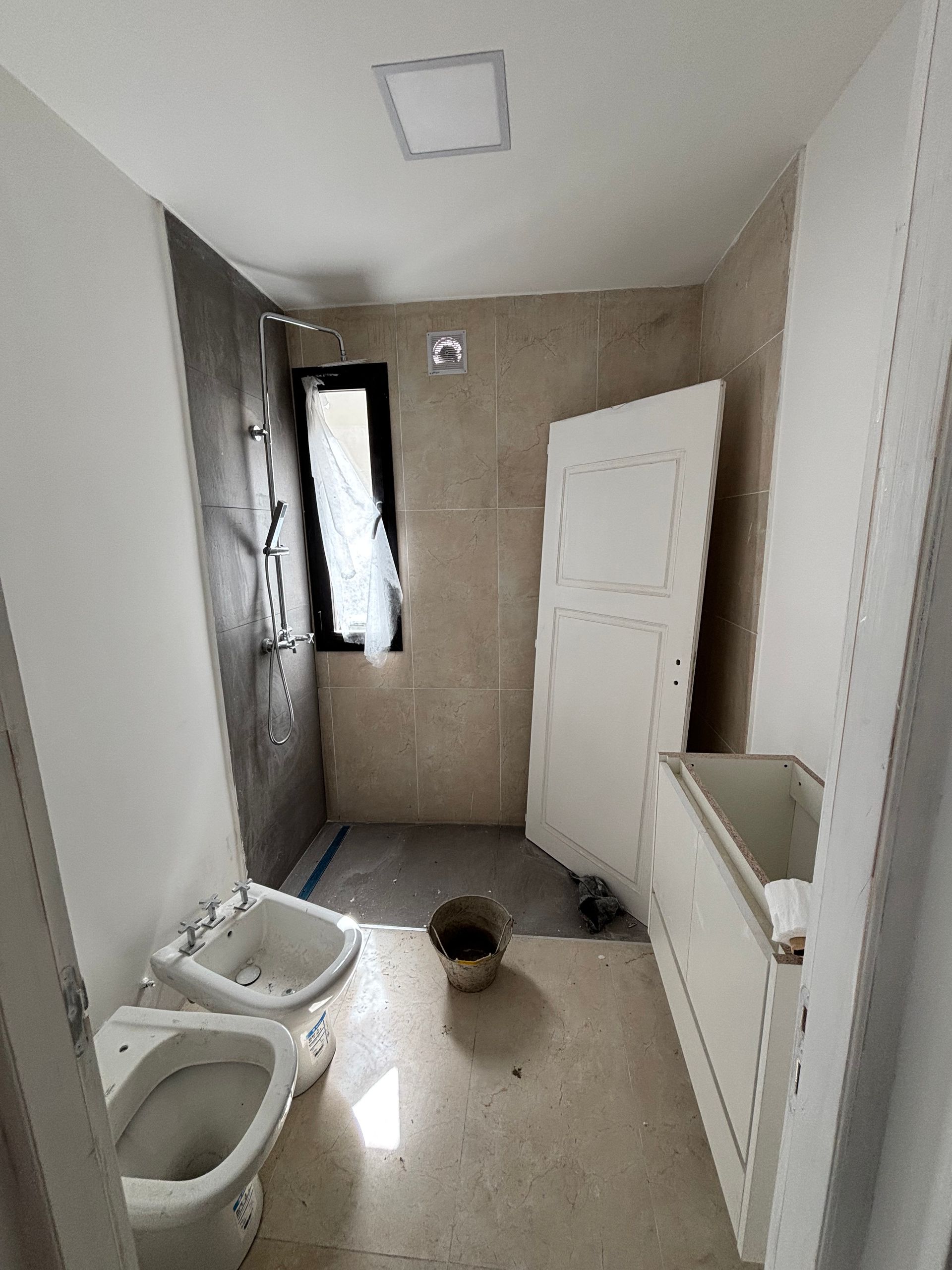Baño en construcción; sanitarios blancos, ducha gris, puerta abierta, sin terminar.