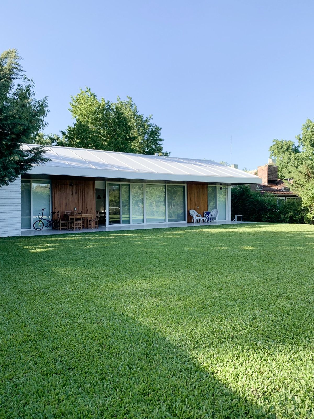Moderna casa de una sola planta con techo plano y grandes ventanales, rodeada de un césped verde en un día soleado.