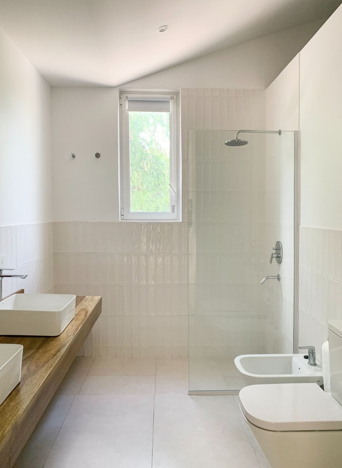 Baño blanco con lavabo, ducha, inodoro y ventana.