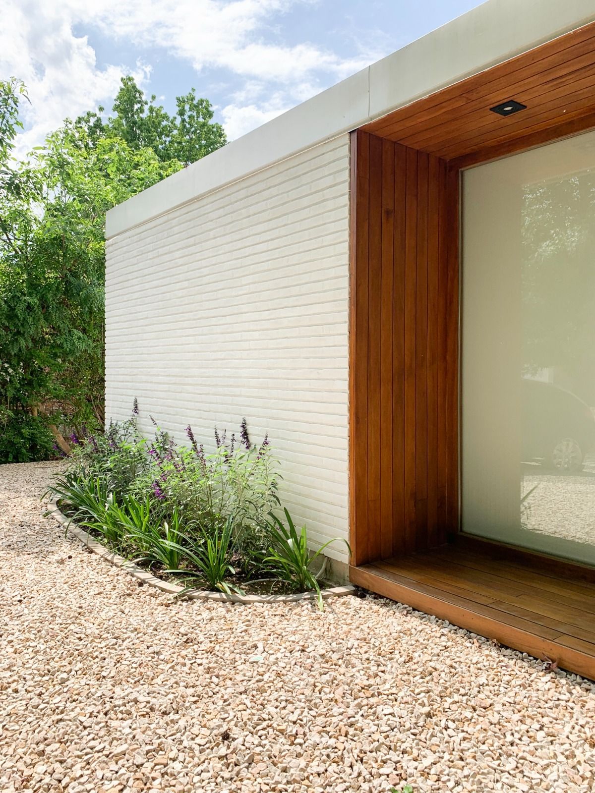 Edificio moderno de ladrillo blanco con entrada de madera, sendero de grava y plantas de lavanda.