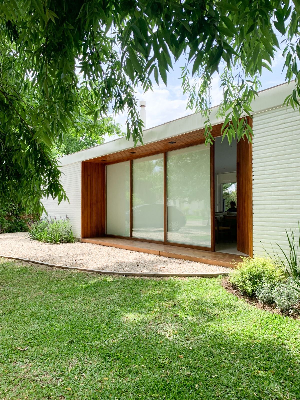 Casa moderna con detalles de madera y puertas corredizas de vidrio, rodeada de césped verde y jardines.