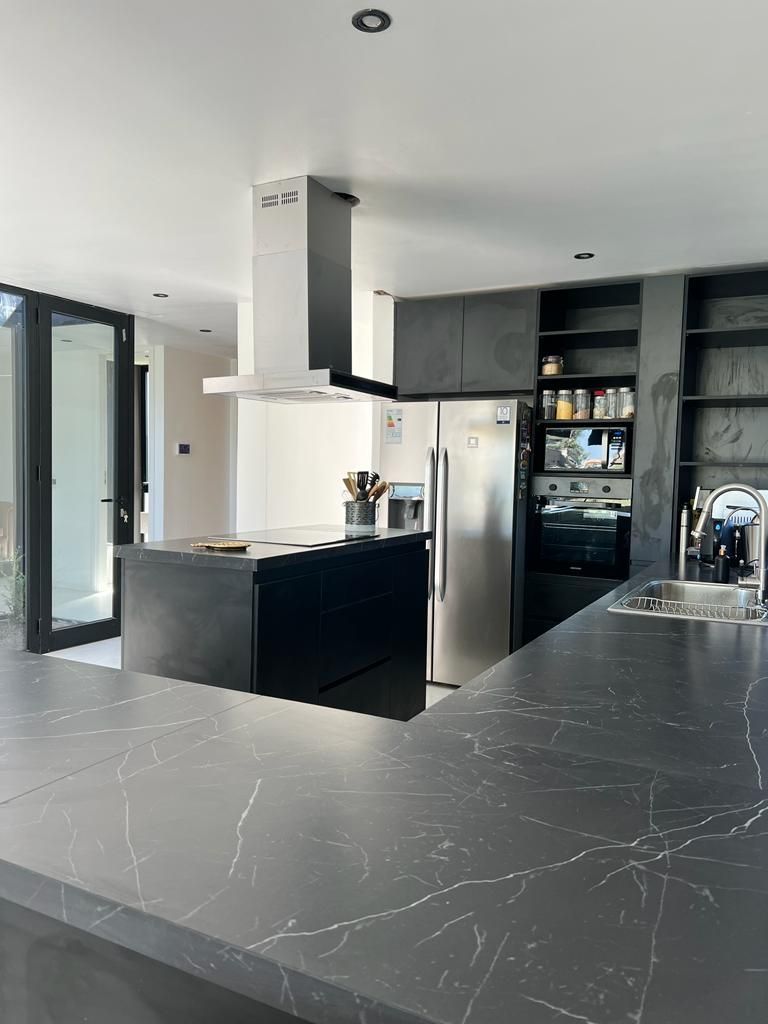 Cocina moderna con encimeras oscuras, isla, frigorífico de acero inoxidable y campana extractora.