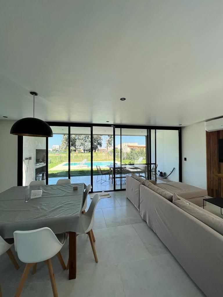 Espacio diáfano con mesa de comedor, sofá y grandes ventanales con vistas a la piscina y al jardín.