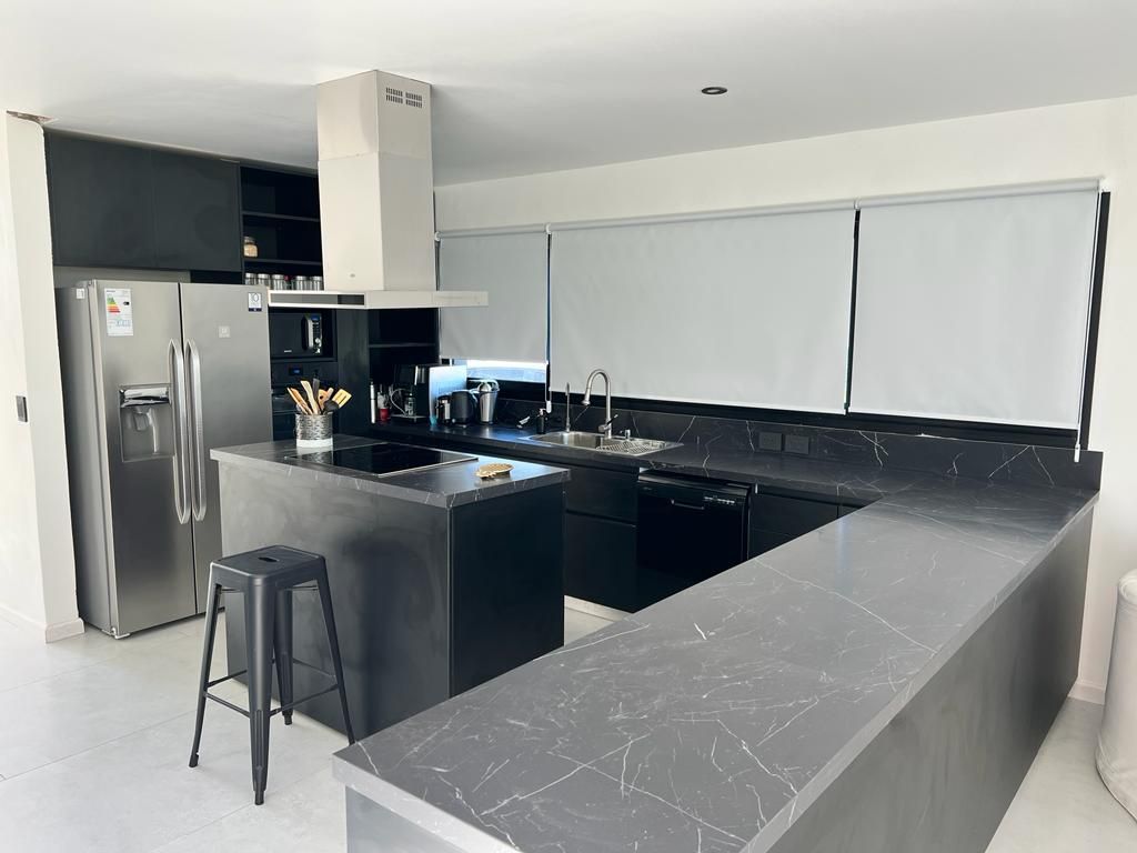 Cocina moderna con encimeras oscuras, electrodomésticos de acero inoxidable y persianas blancas.