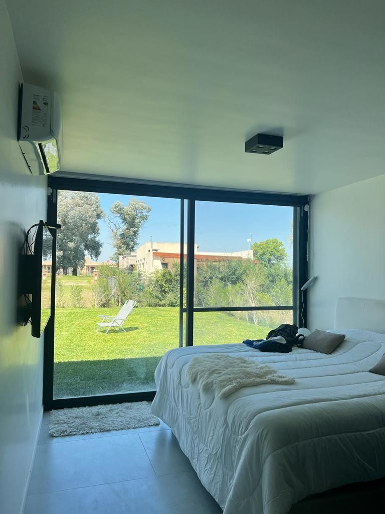 Dormitorio con gran ventanal con vistas al jardín, cama, televisión y aire acondicionado.