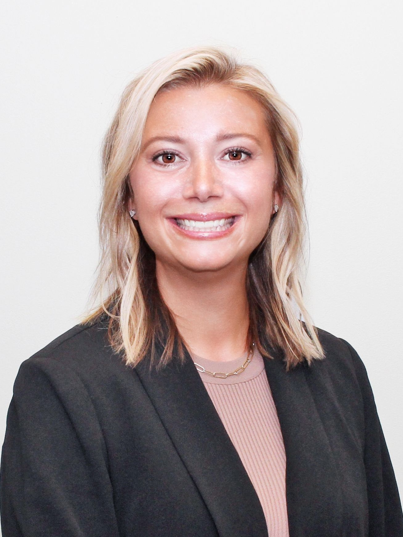 Woman in a black blazer smiles at the camera, light skin, light blonde hair.