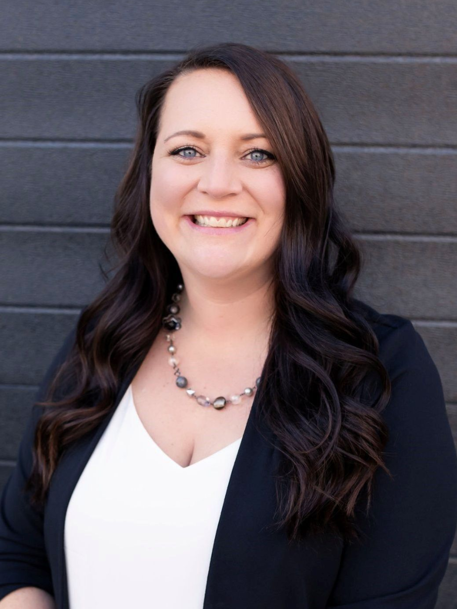 Woman with wavy brown hair wearing a black blazer and a white shirt.