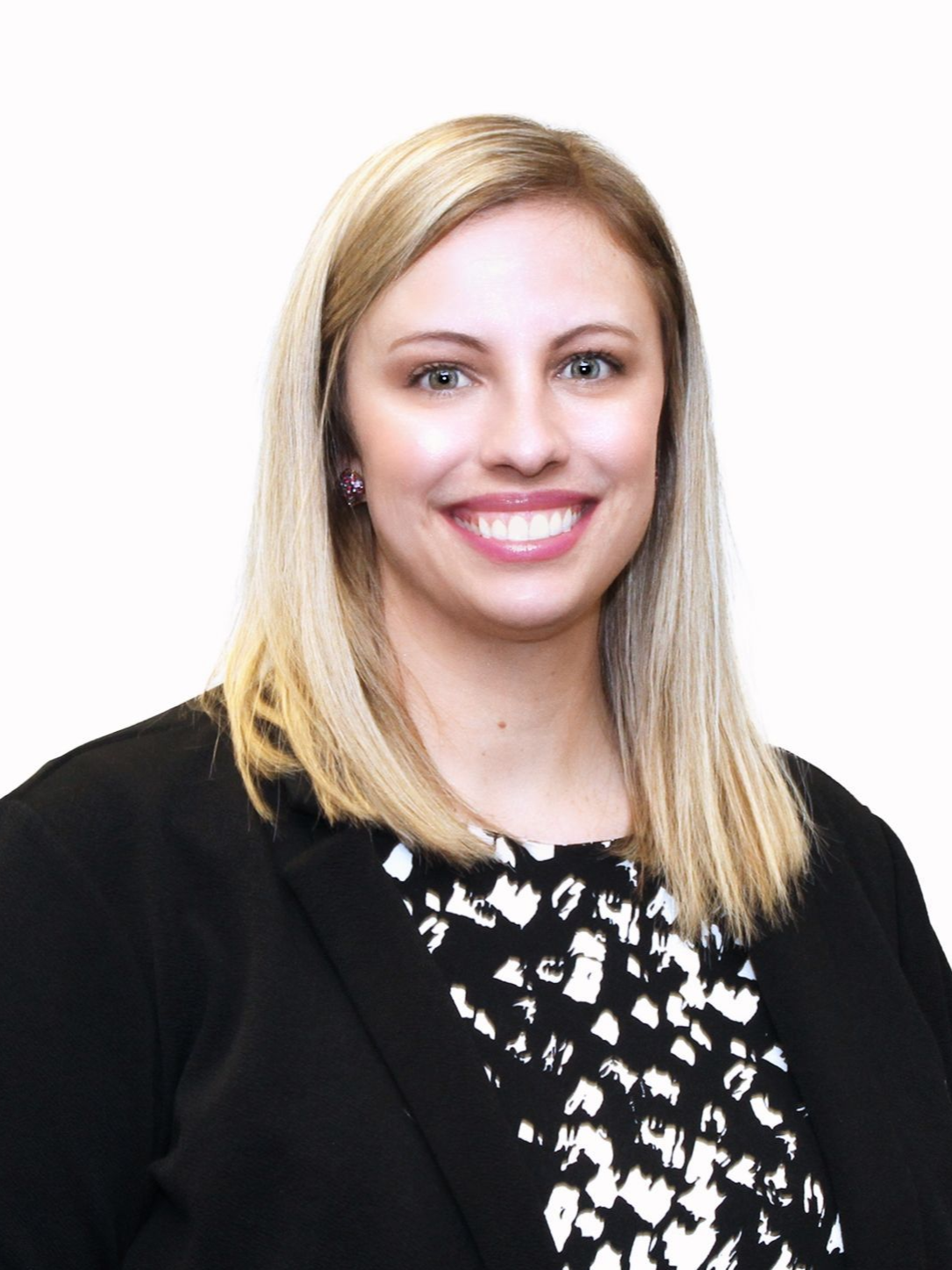 Woman with blonde hair smiling, wearing a black blazer over a black and white patterned top.