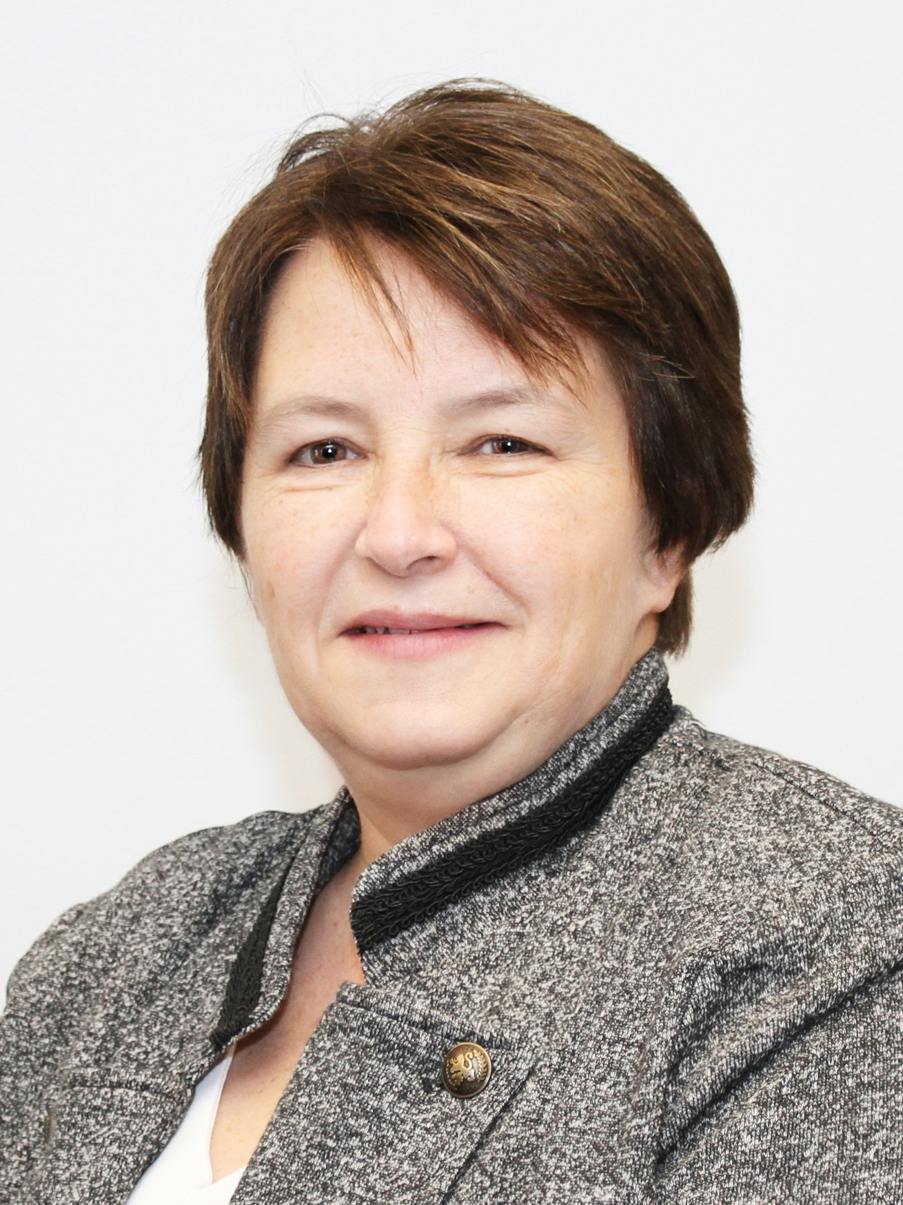 Woman with short brown hair, wearing a gray blazer, smiling against a plain white background.