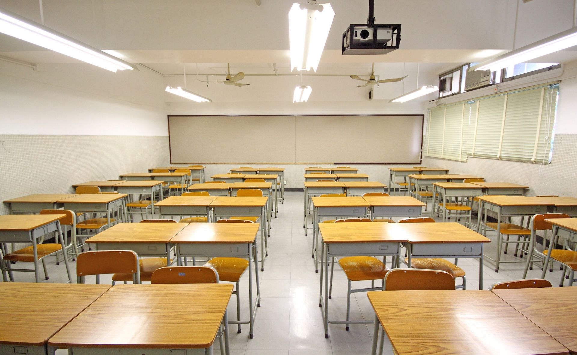 Empty classroom with rows of desks, a whiteboard, and a projector.