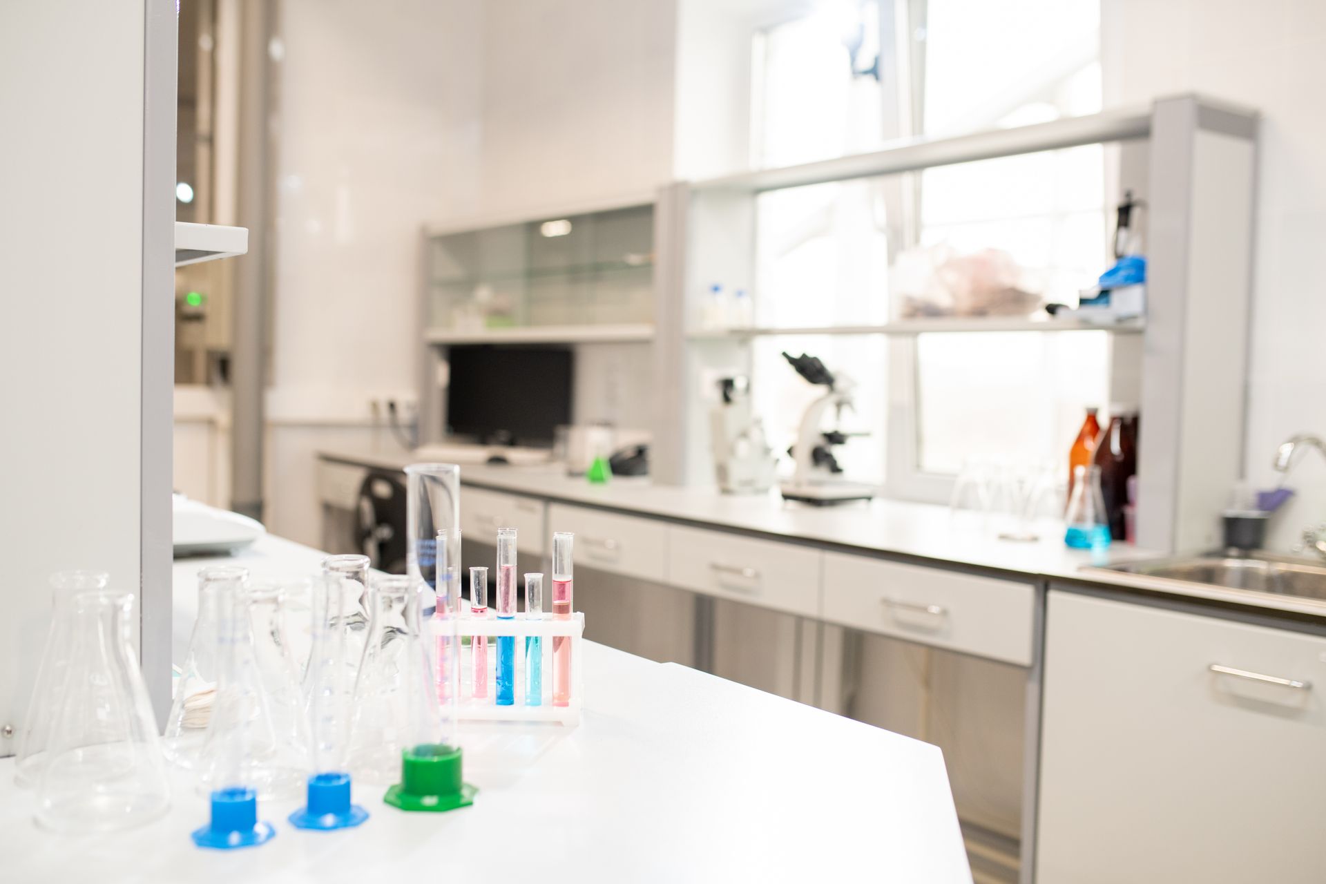 Laboratory bench with beakers, test tubes, and colored liquids; cabinets and windows in background.