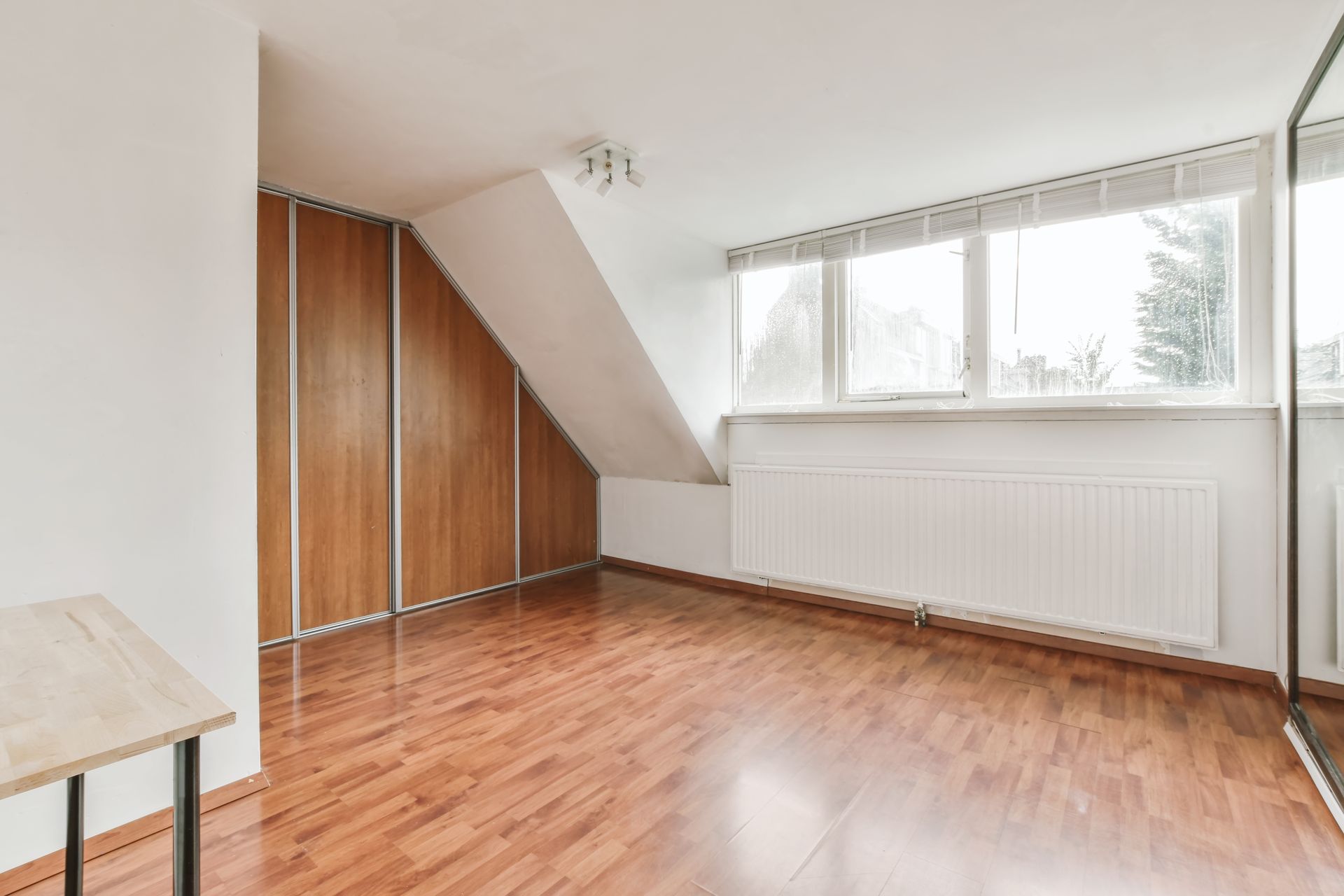 Empty room with slanted ceiling, hardwood floor, large windows, and wooden closet doors.