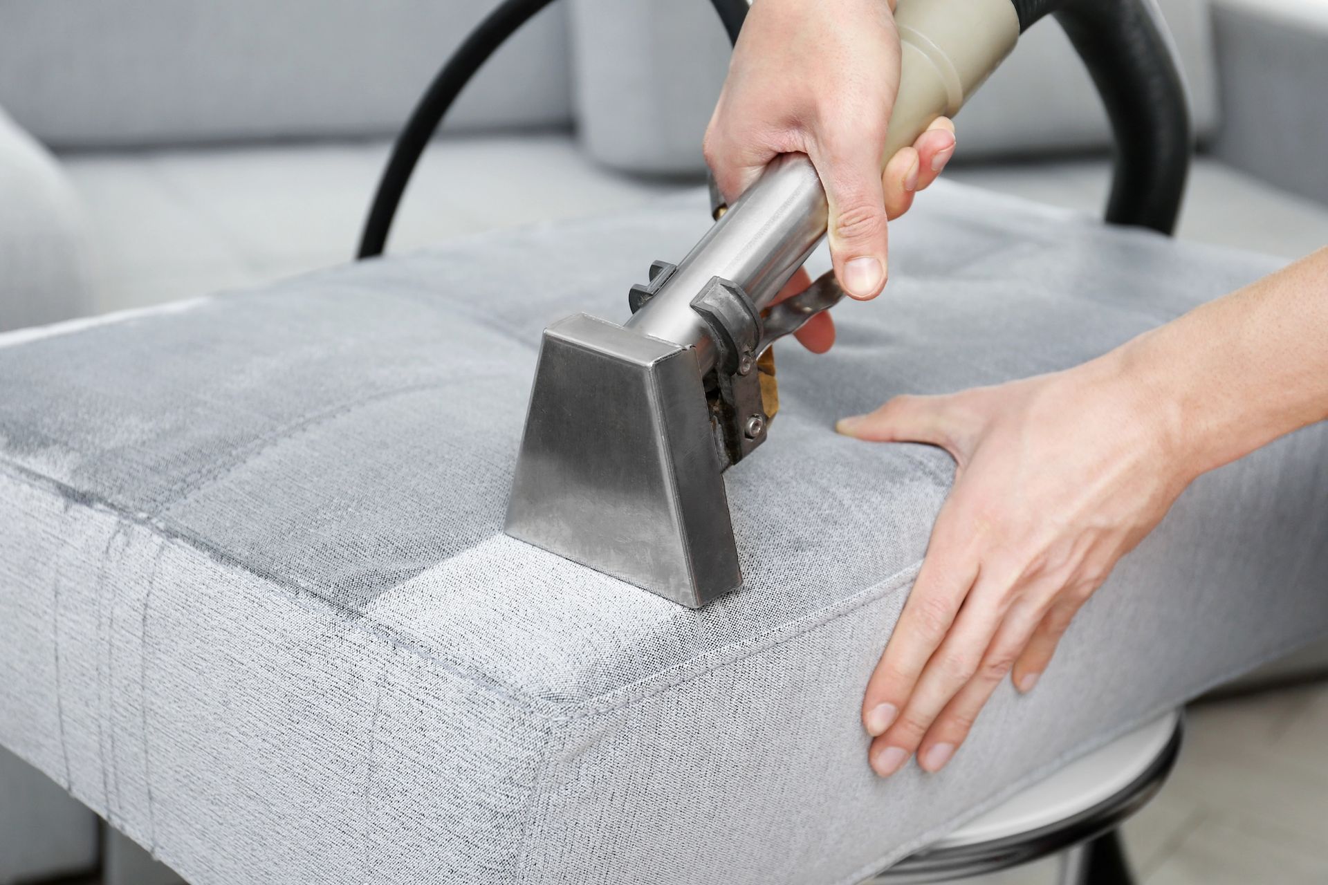 Person using upholstery cleaning tool on a gray cushion, indoors.