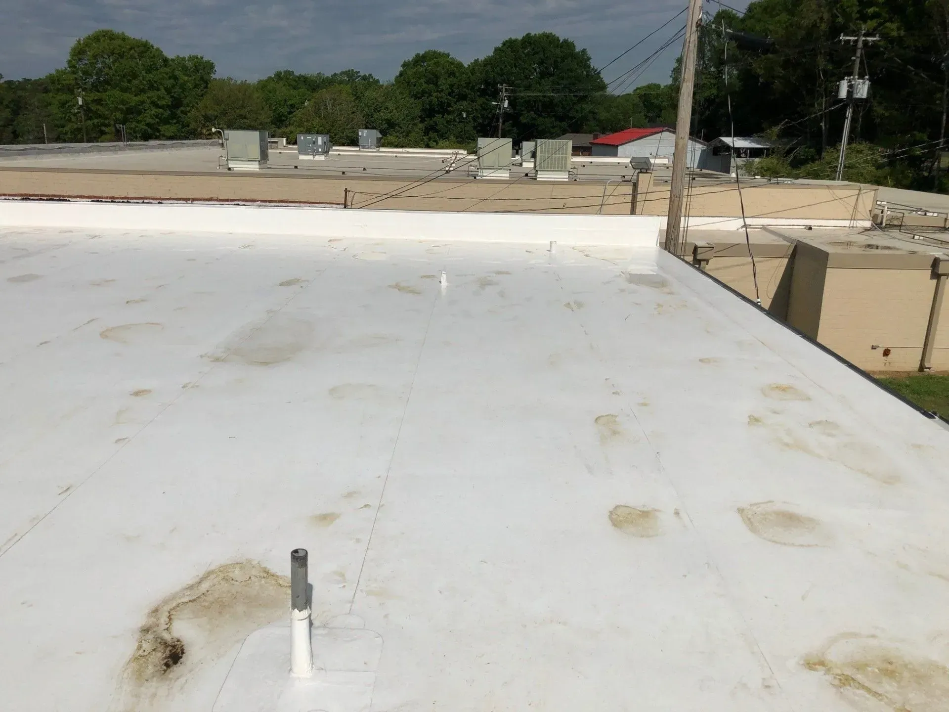 White rooftop with vents overlooking a road and trees under a cloudy sky