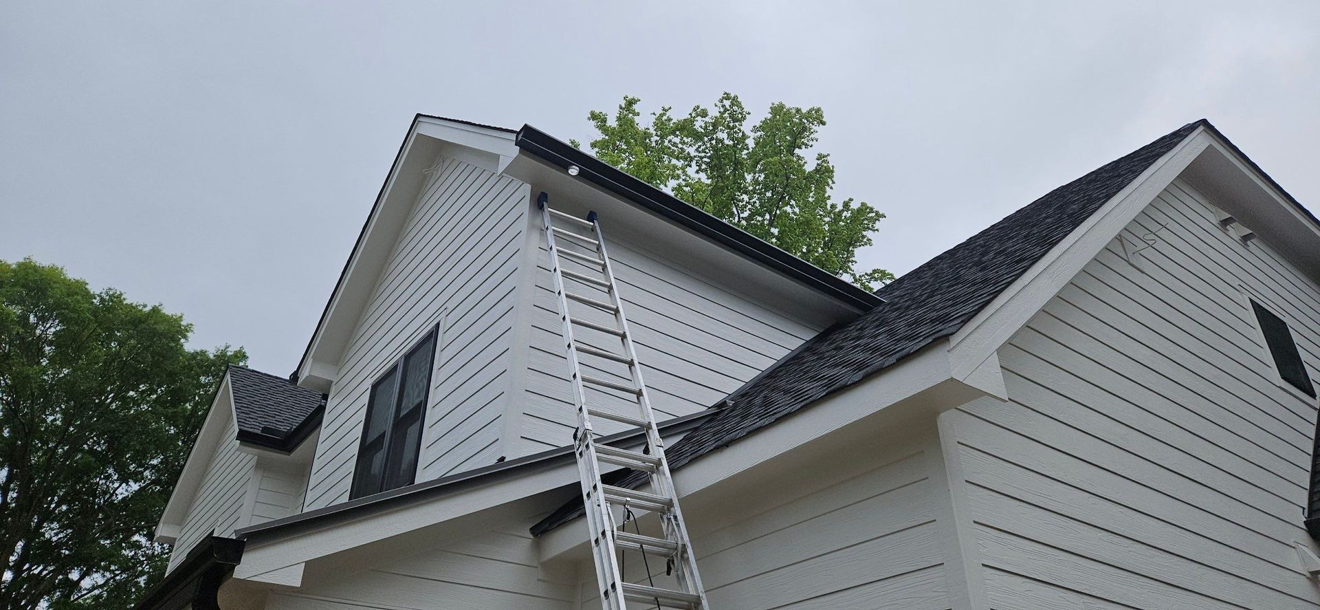 Ladder leaning against a white house roof near a dormer and trees