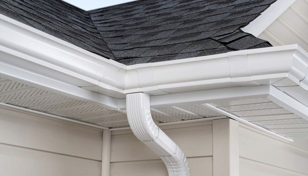 White gutters on a house with a dark shingle roof and light beige siding.