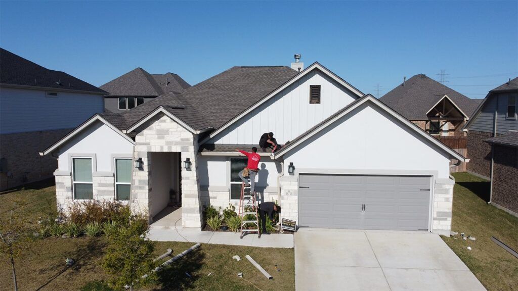 Two workers on a ladder repairing a gutter on a white house with a grey garage door in Houston, TX.