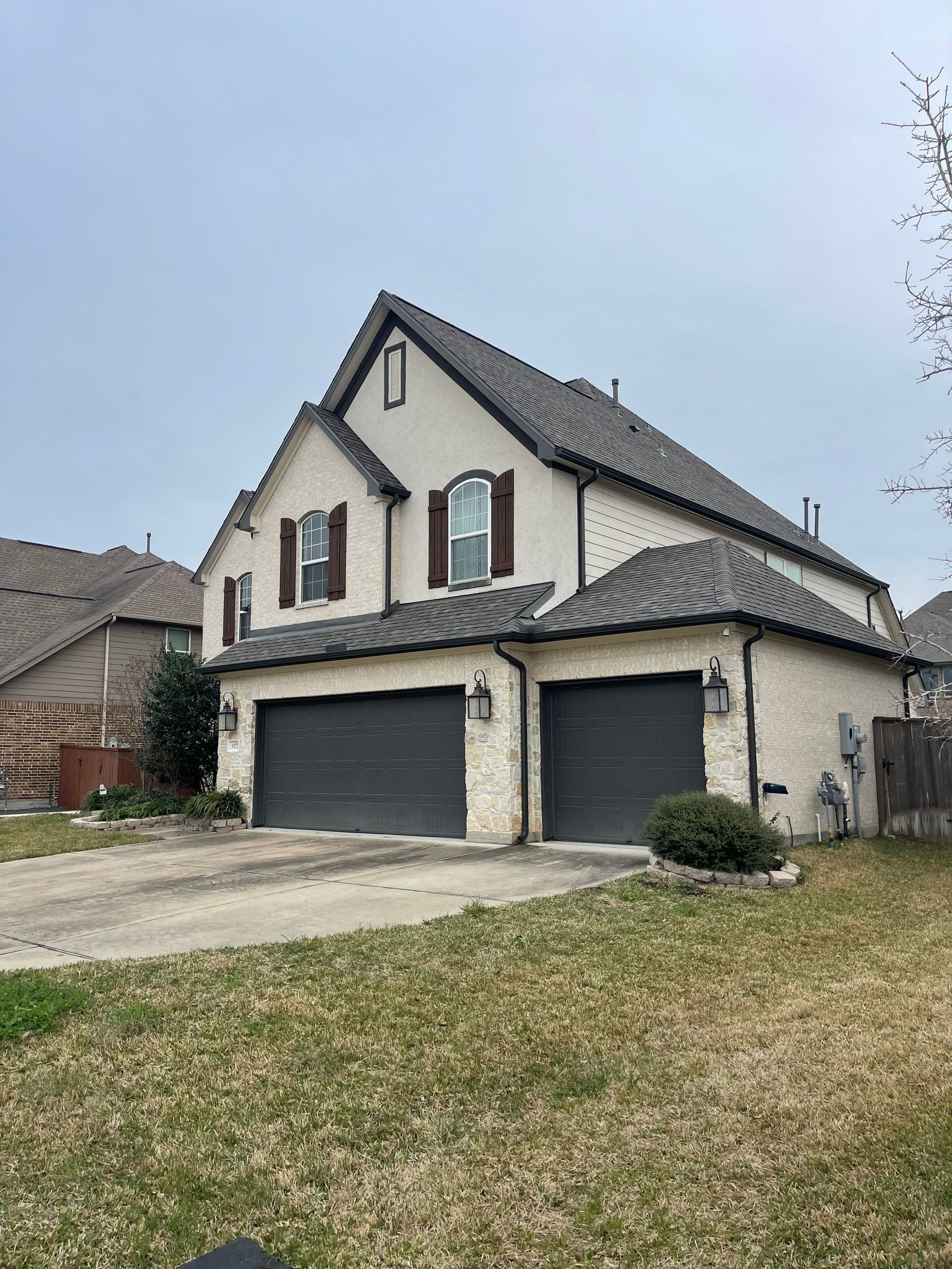 Two-story house with grey garage doors and maintained gutters with brown trim under an overcast sky in Houston, TX.