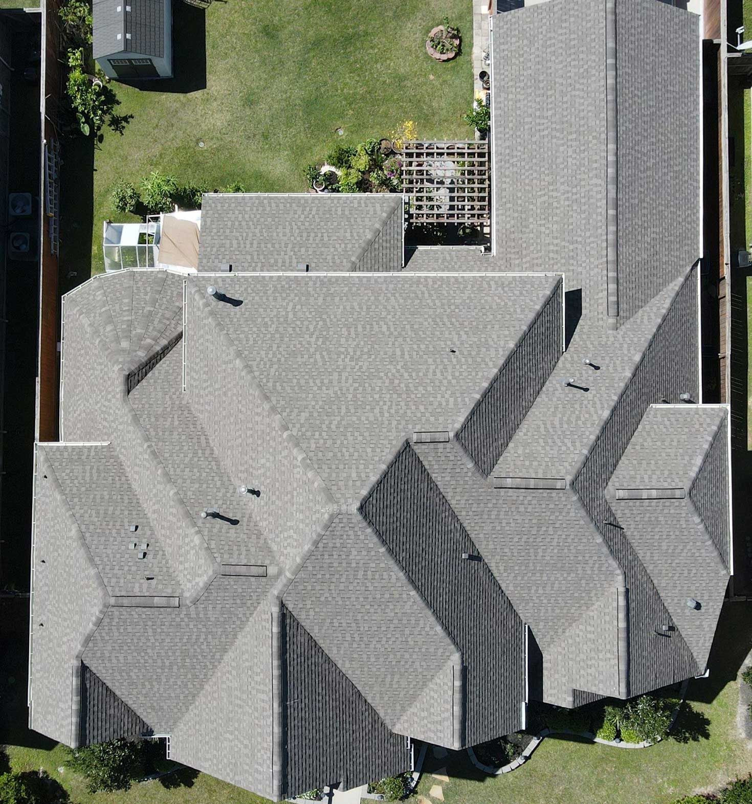 Aerial view of a gray-roofed house with a backyard lawn and surrounding trees.