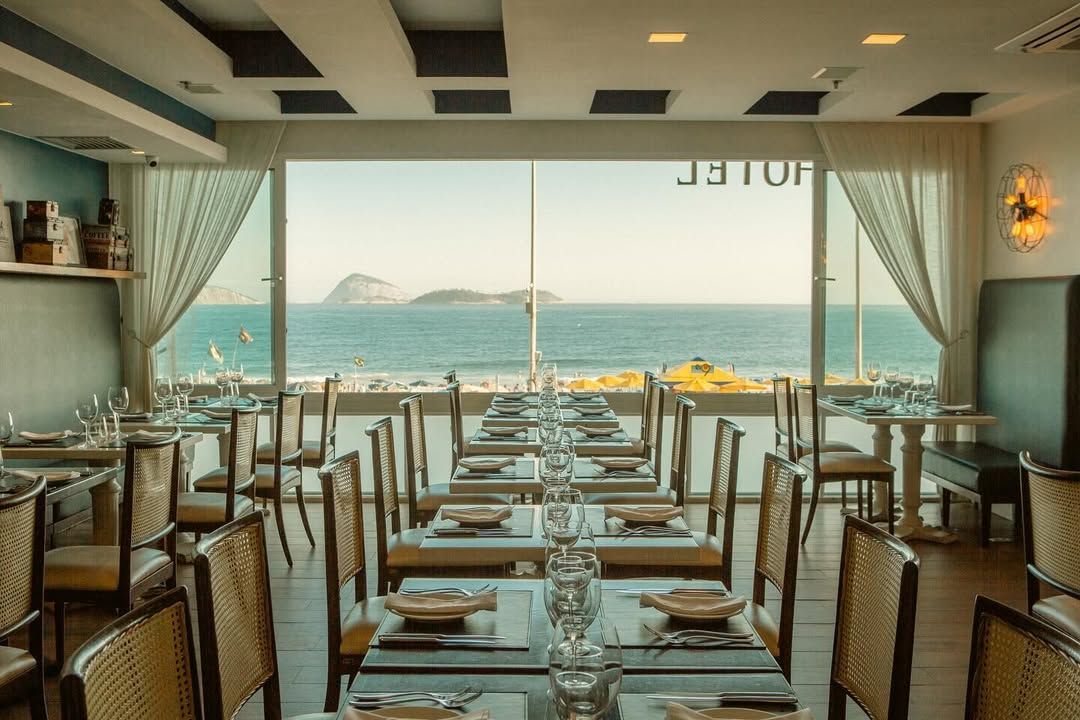 Um restaurante com mesas e cadeiras e vista para o oceano. Sol de Ipanema Hotel