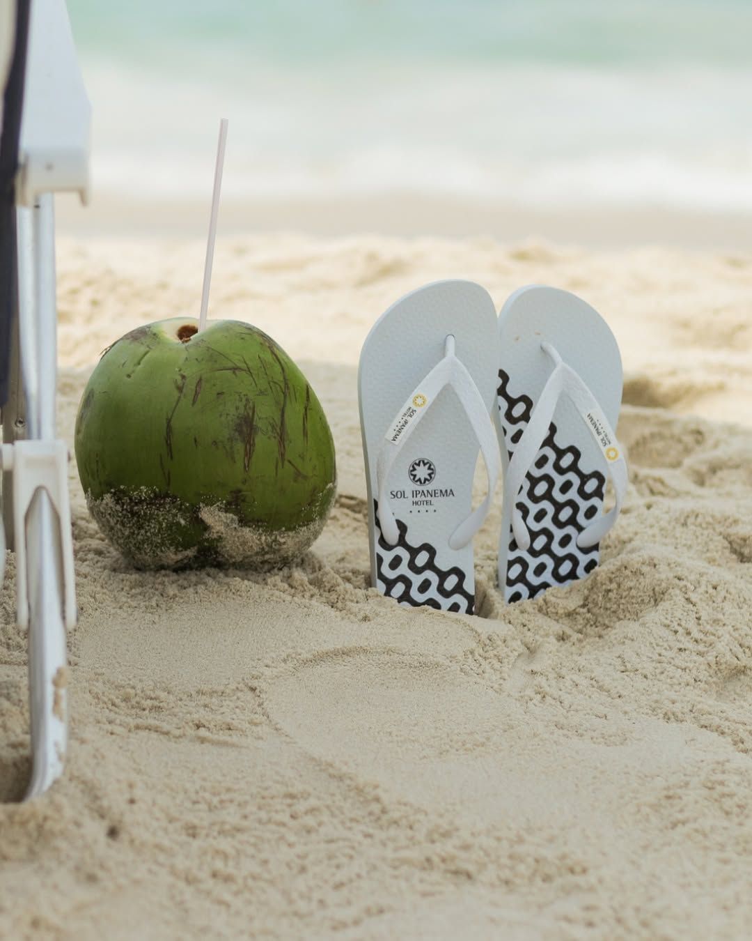 Um par de chinelos na praia ao lado de um coco Sol de Ipanema Hotel