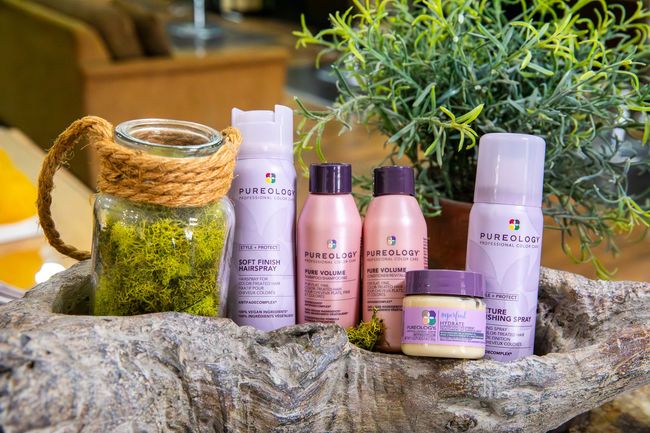 Hair care products in purple and pink bottles, arranged with greenery in a rustic setting.