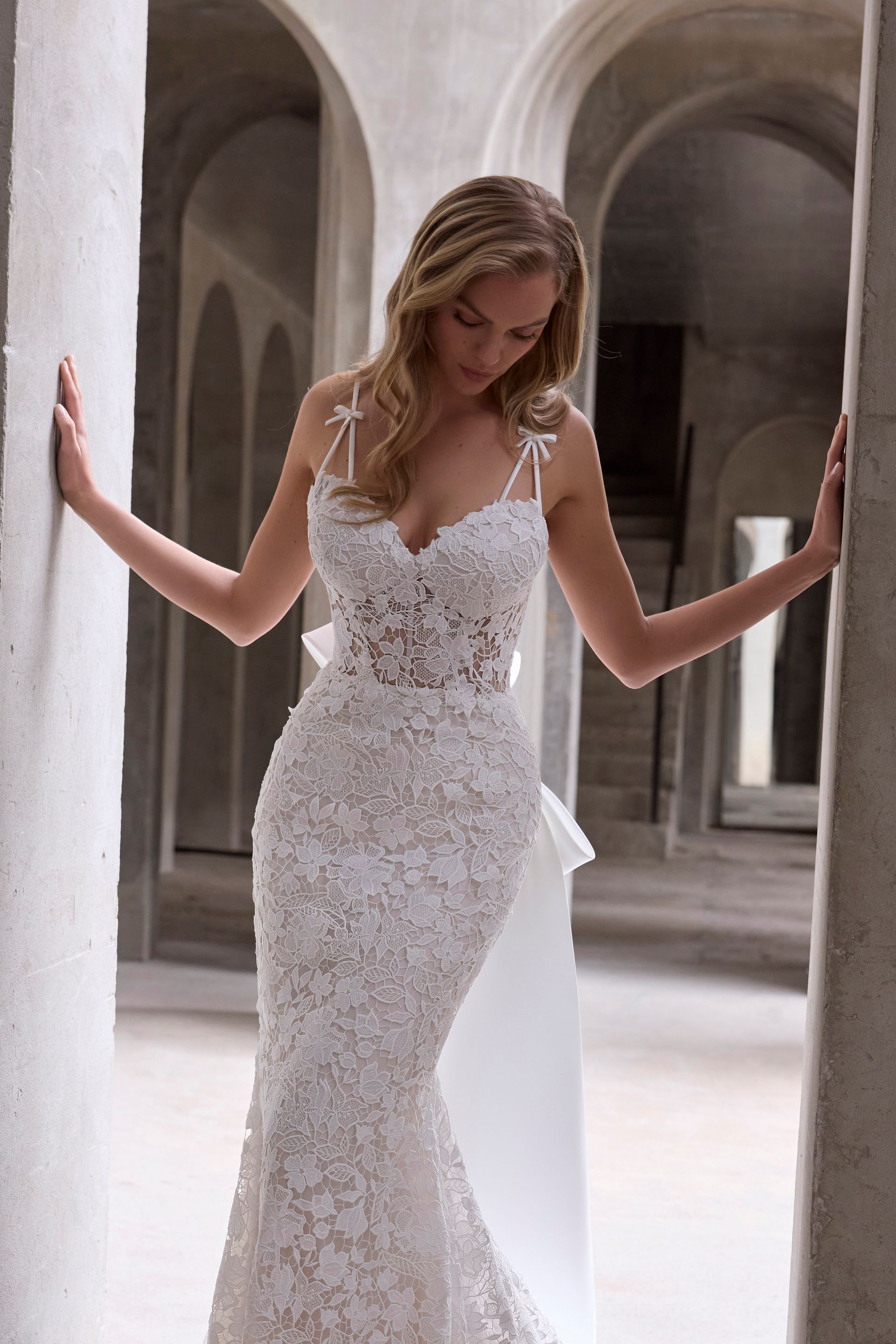 Woman in white lace wedding dress poses between stone columns.