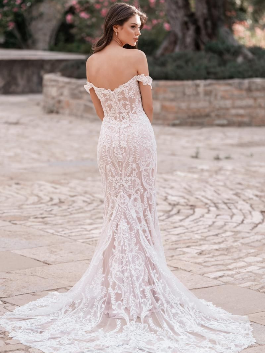 Woman in white lace off-shoulder wedding dress, standing outdoors with a long train.