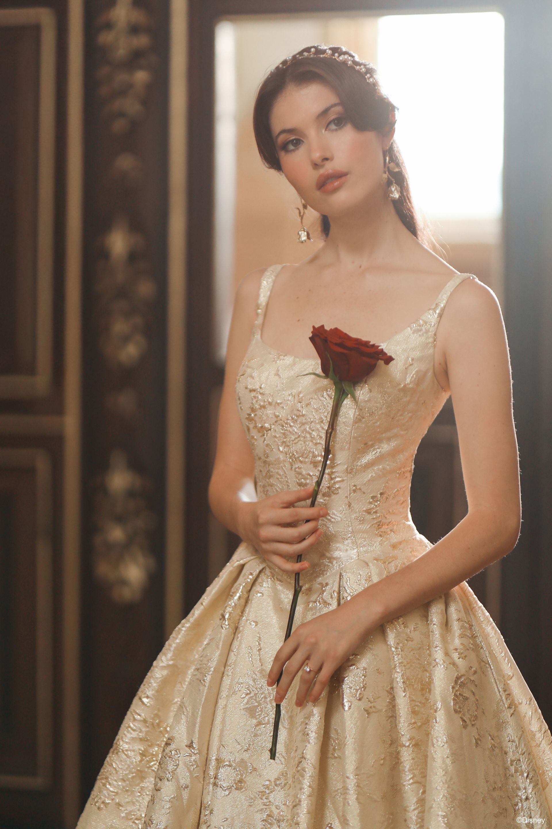 Woman in a beaded white wedding dress, side profile, standing indoors with wood panel doors.