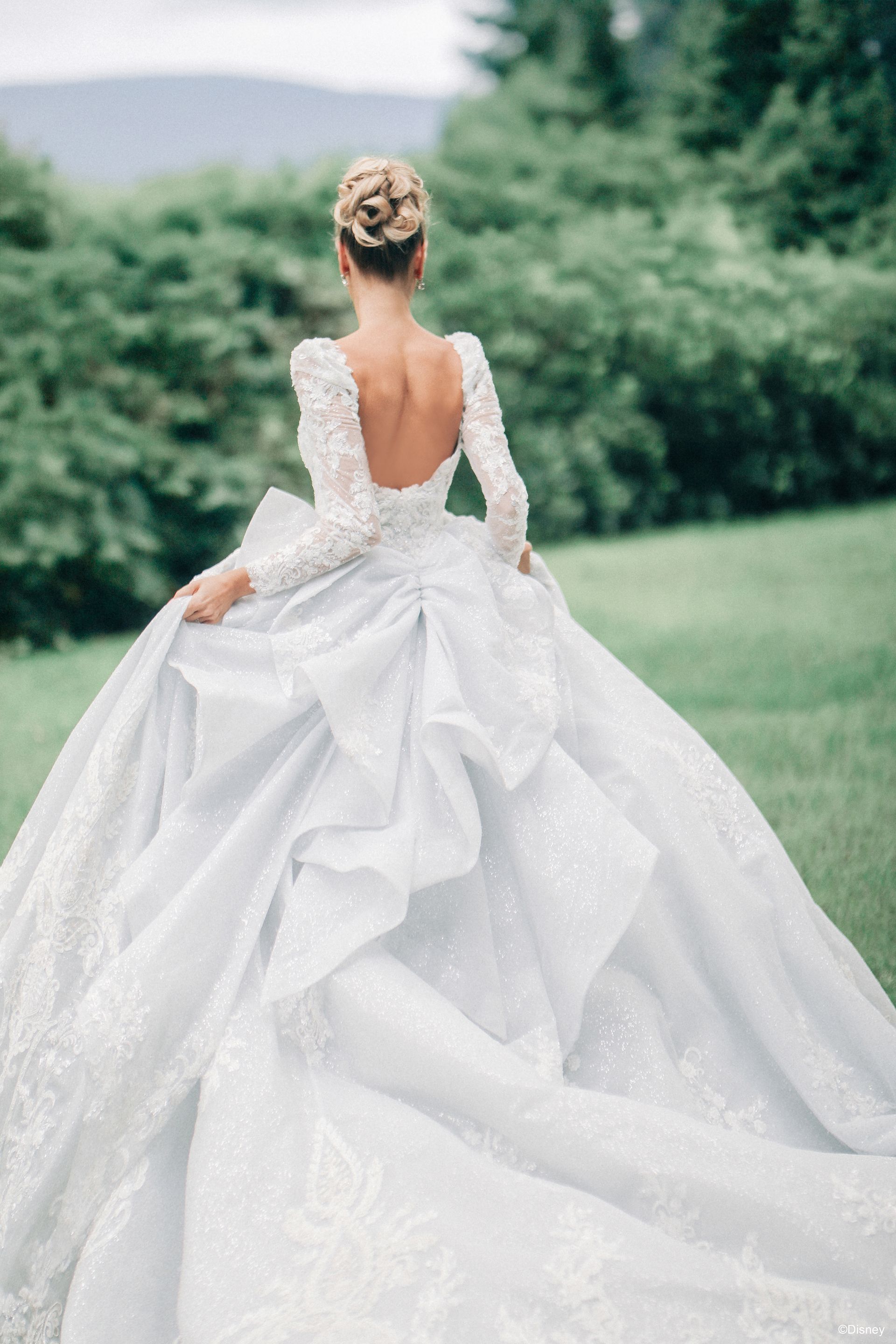Woman in white, one-shoulder wedding dress, with floral accent, standing in front of ornate, dark doors.