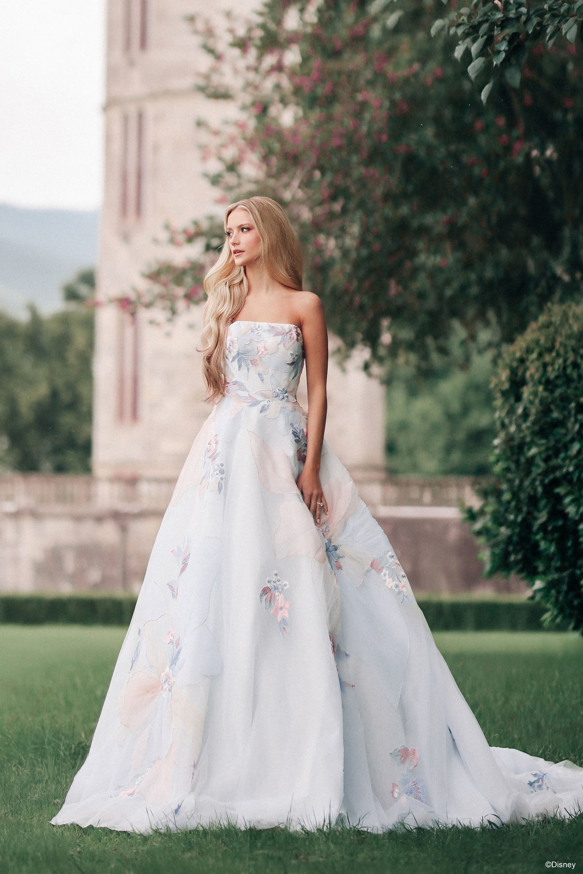 Bride in a white lace gown smiles, covering her mouth. She stands in a large room with patterned flooring.