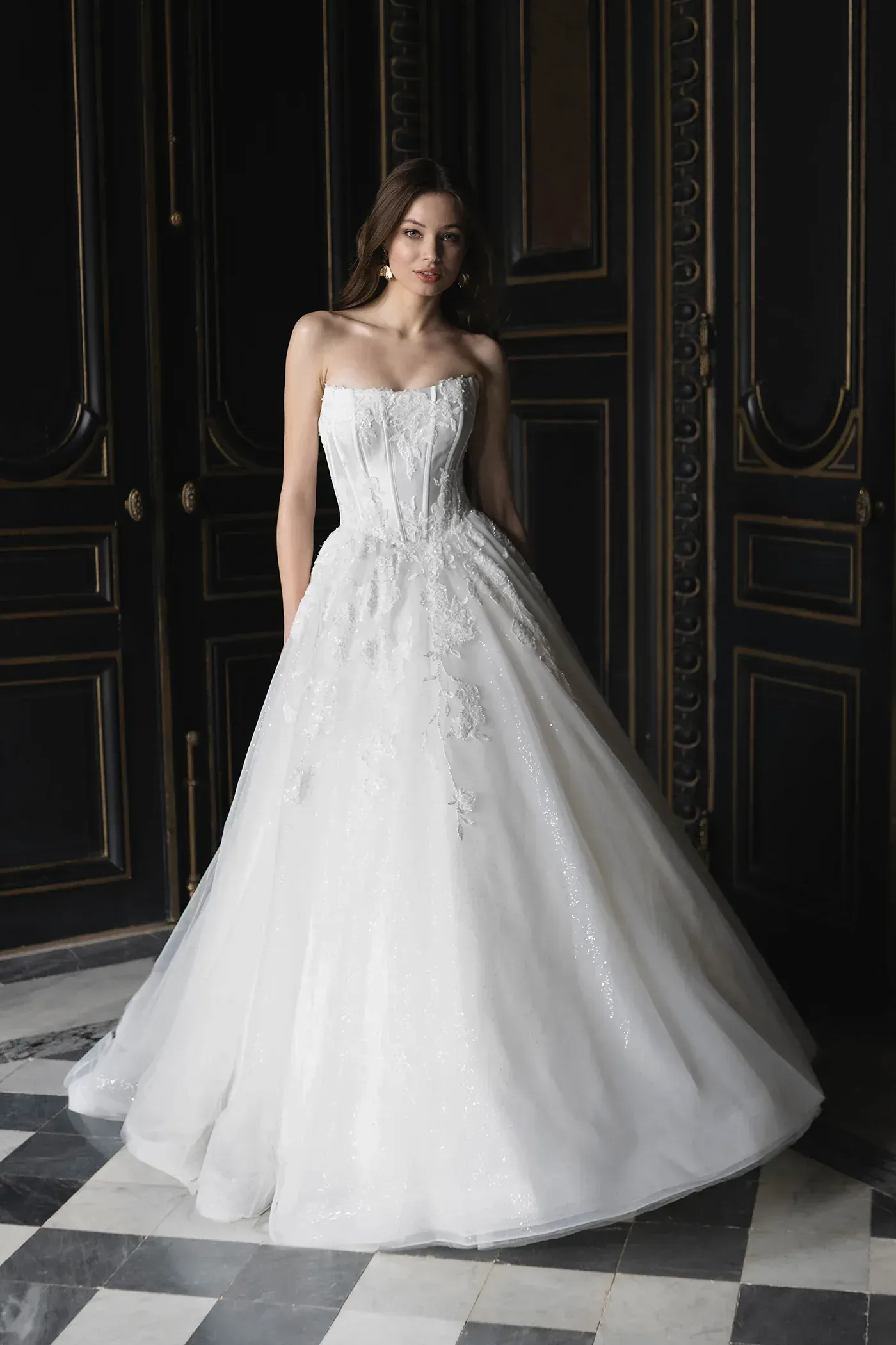 Woman in a white strapless ballgown, standing in a room with black and gold doors.