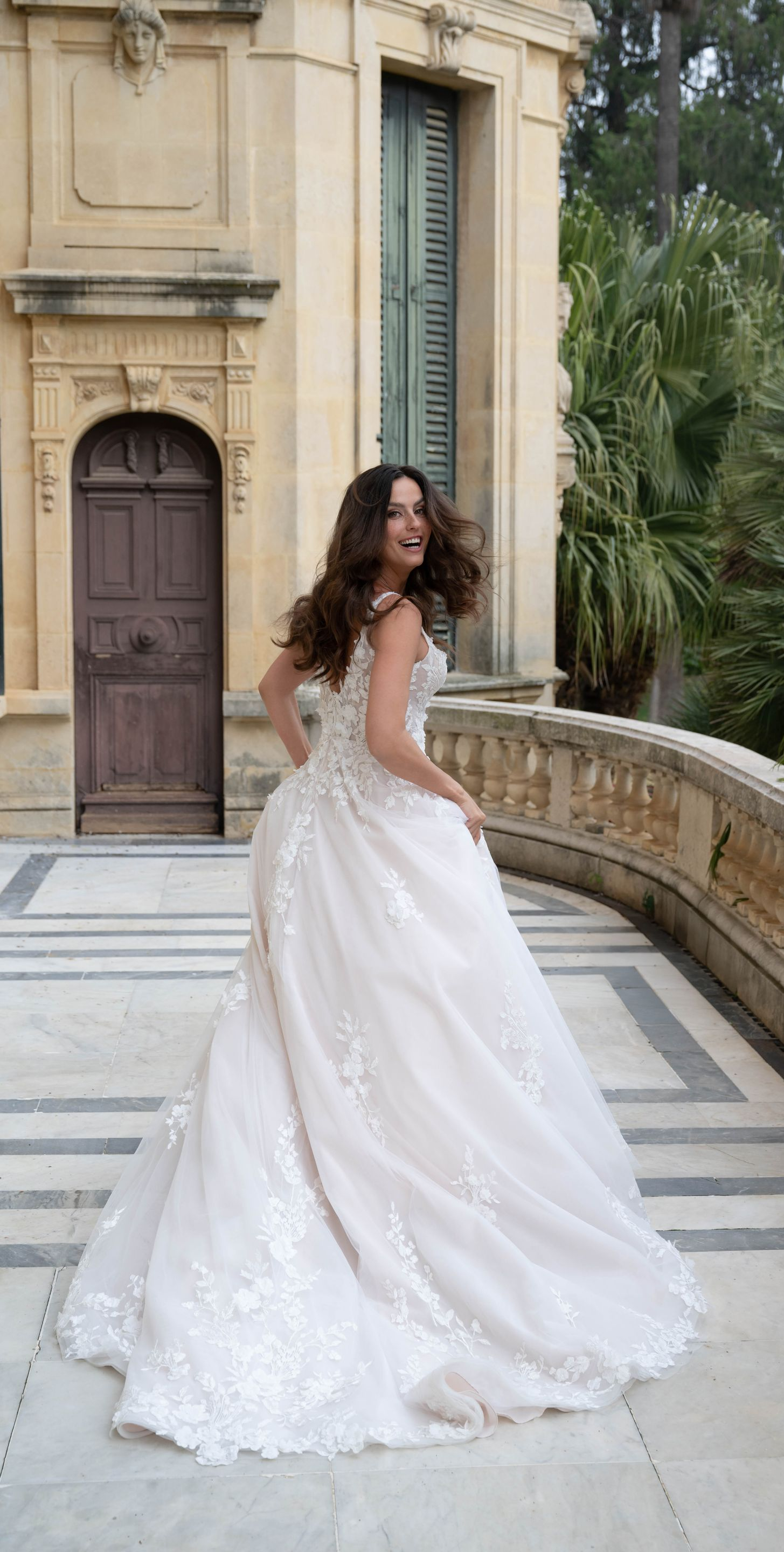 Woman in a white wedding dress twirling on a stone patio with a European-style building in the background.