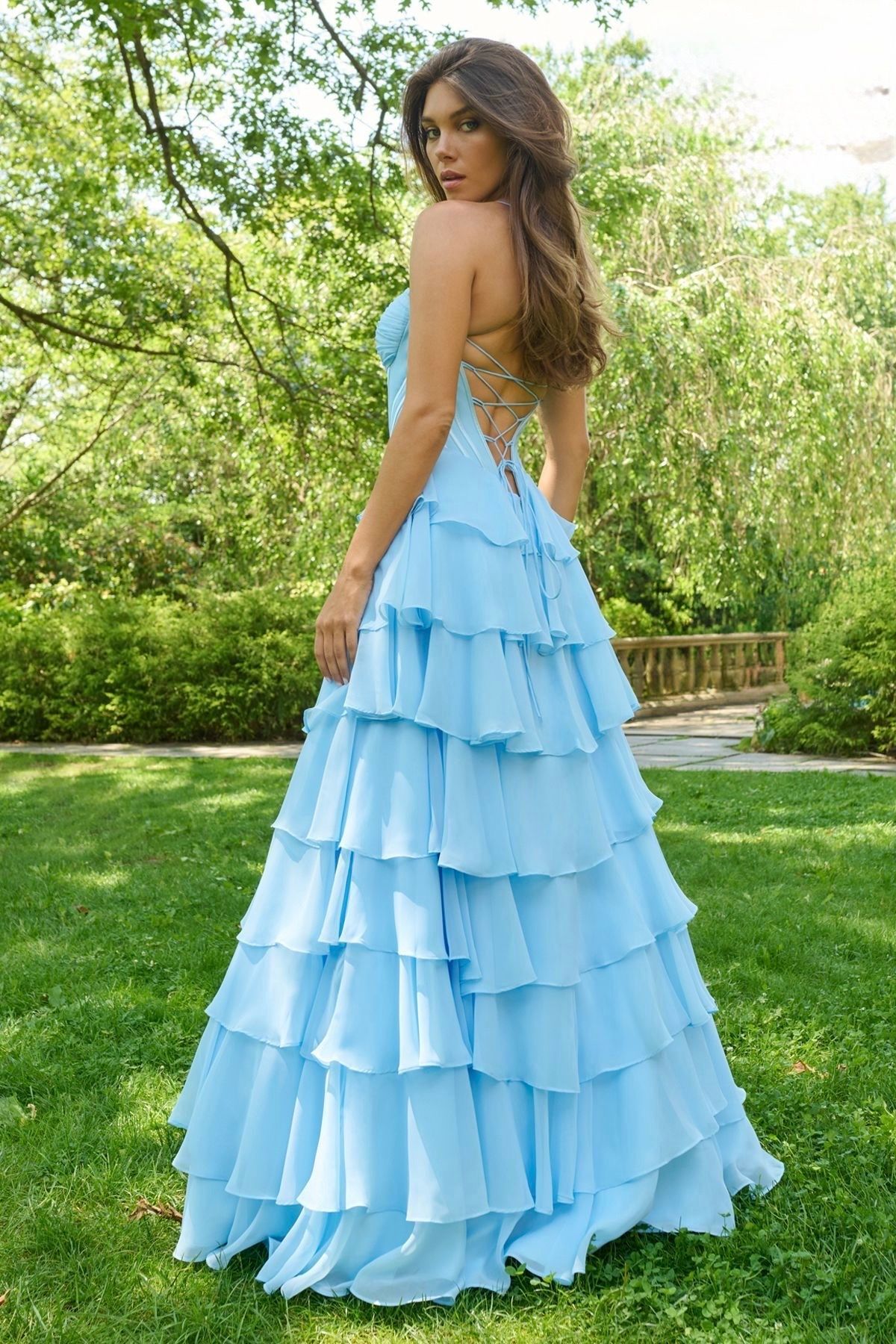 Woman in a light blue tiered formal dress, standing outdoors in a garden setting.
