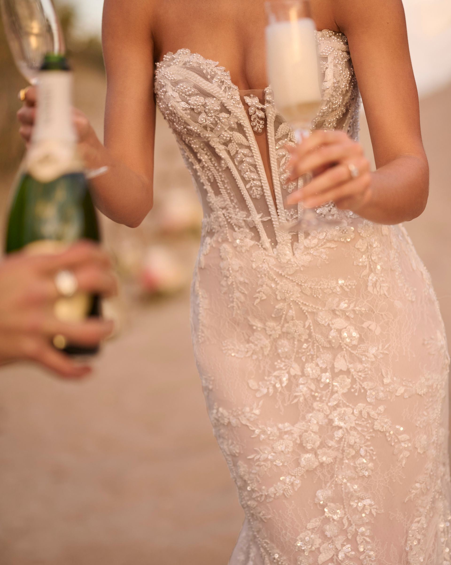 Woman in a beaded wedding dress pours champagne.