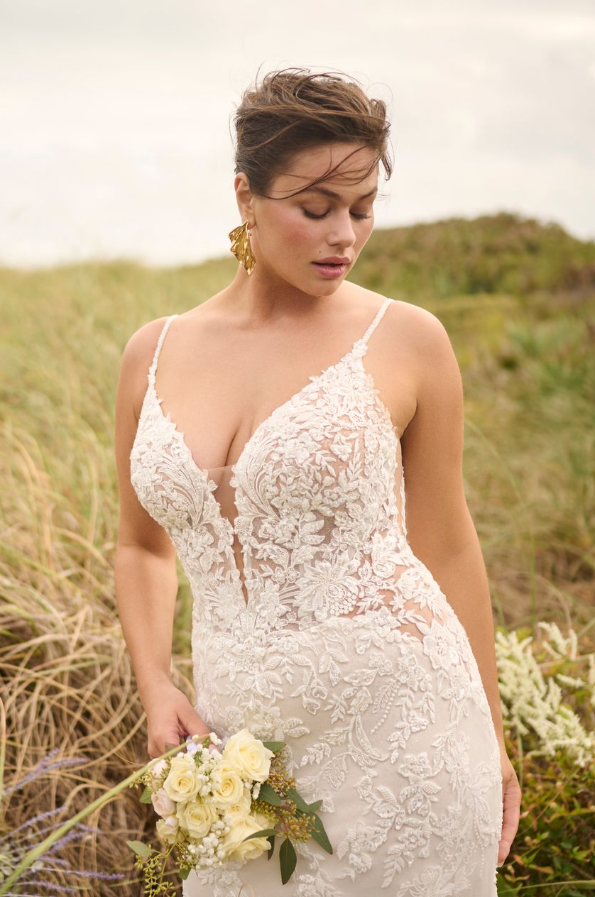 Bride in lace wedding dress, holding flowers, outside.