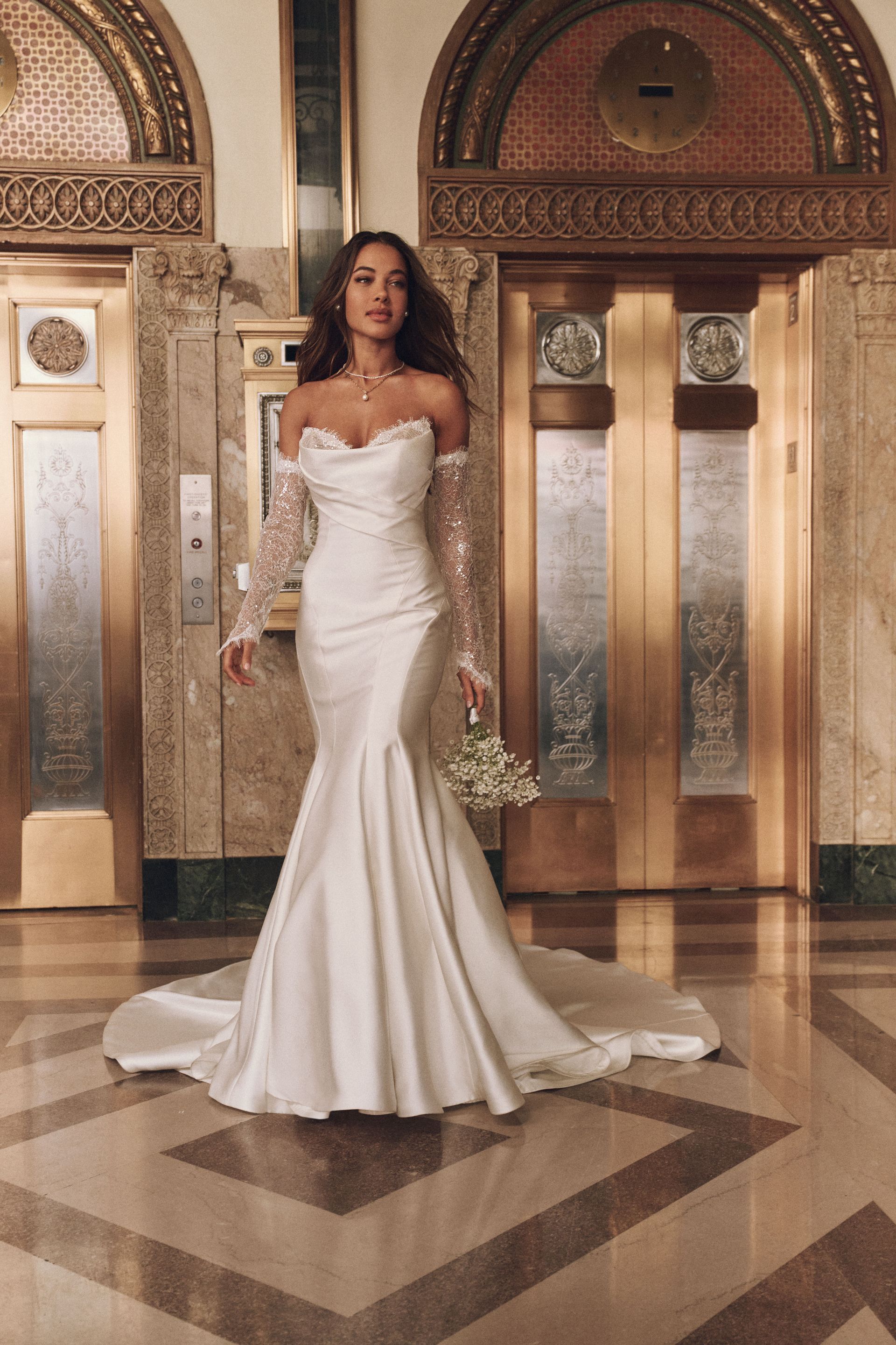 Bride in white gown, holding bouquet, in a grand building with elevators.