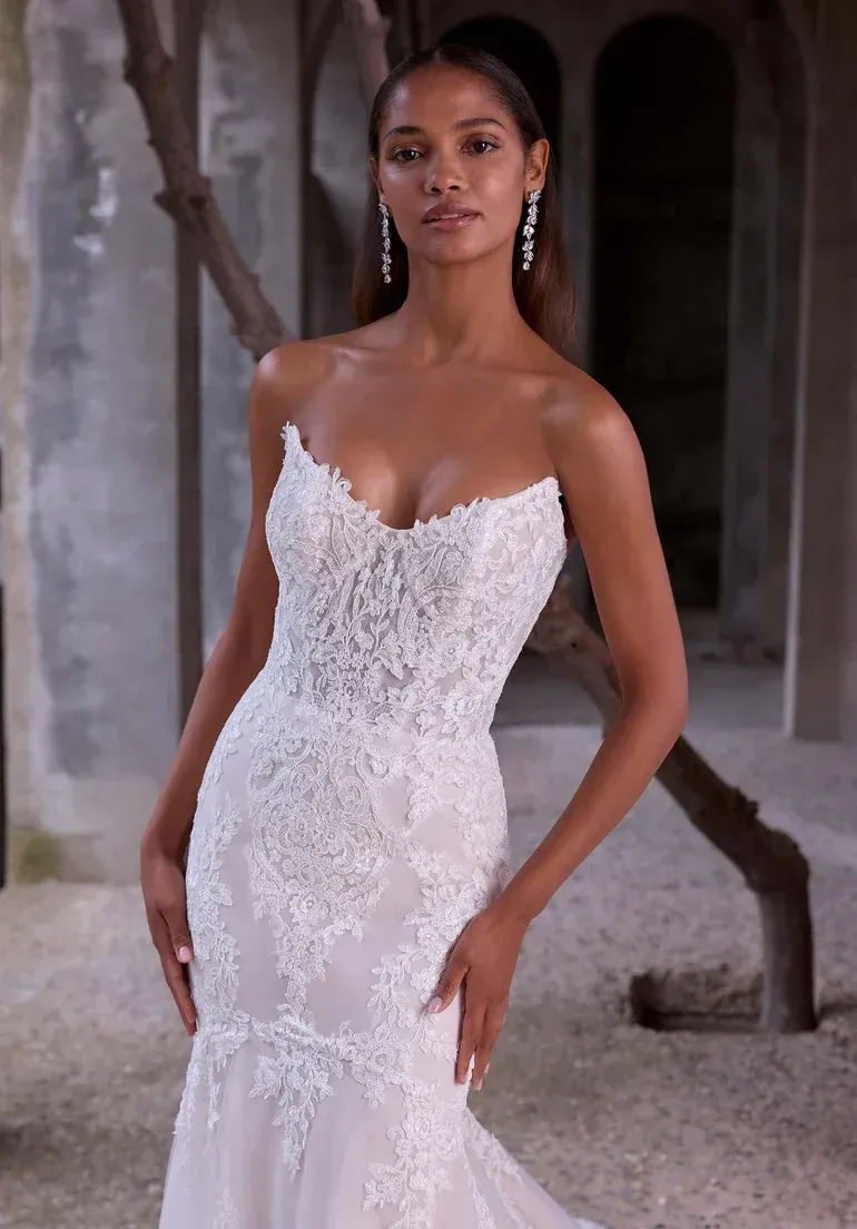 Woman in strapless white lace wedding dress, standing outdoors.