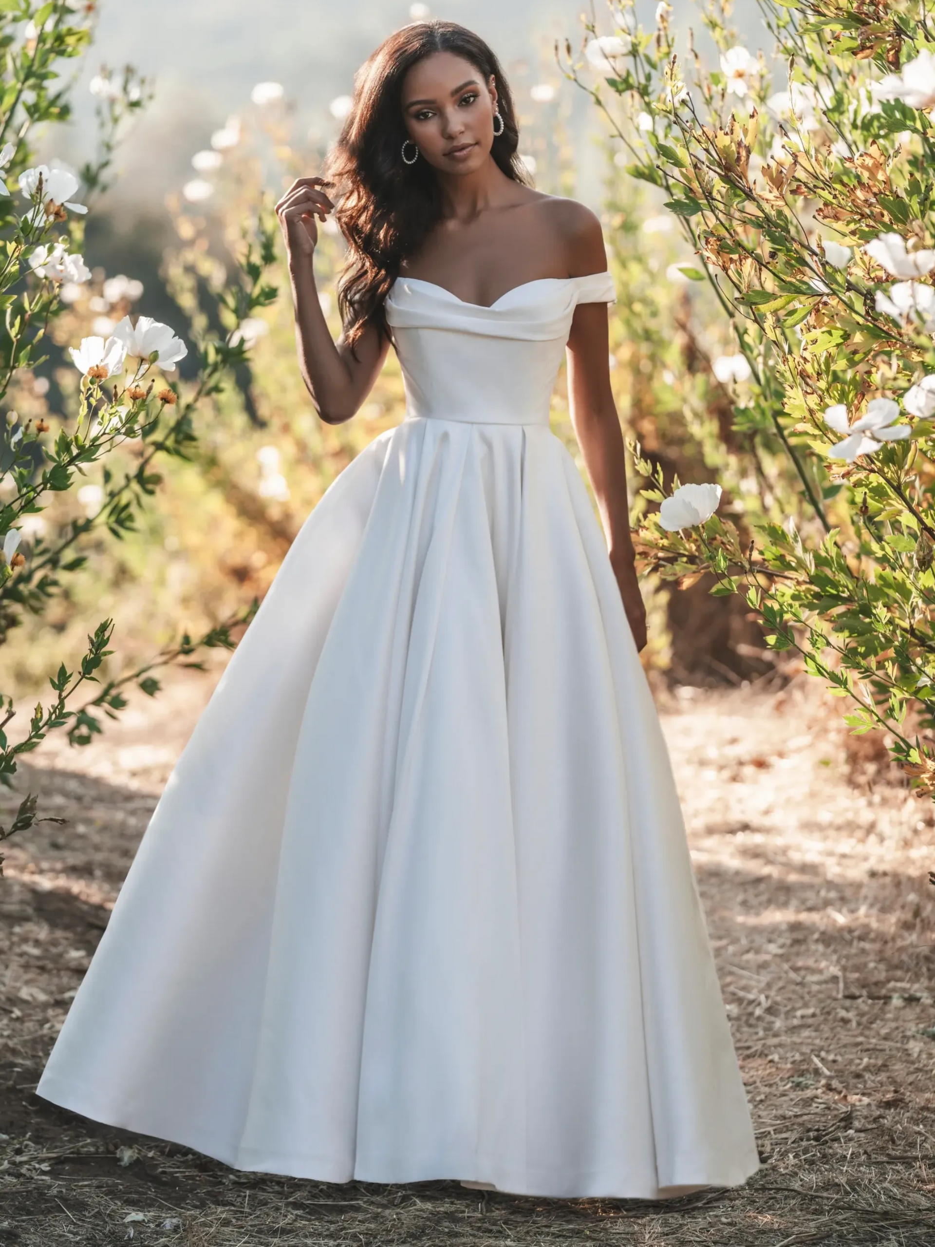 Woman in an off-the-shoulder white wedding dress stands outside.